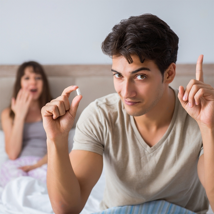 Erectimus for Men instant erection pills. Man in bed with wife about to take the pill.
