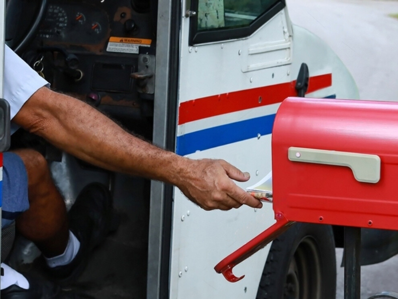 USPS van with driver delivering package into letterbox