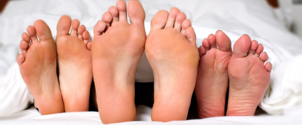 Humorous image of the bare feet of a man and two women in bed sticking out from under the bedclothes conceptual of a threesome, orgy, swingers or sexual cheating